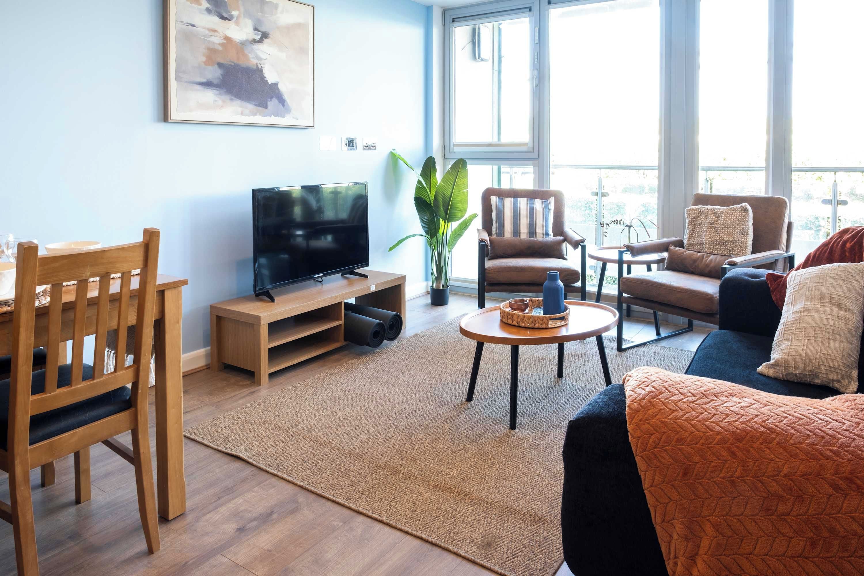 Un salon moderne avec un téléviseur à écran plat posé sur un meuble en bois, une table basse, un canapé et un fauteuil.