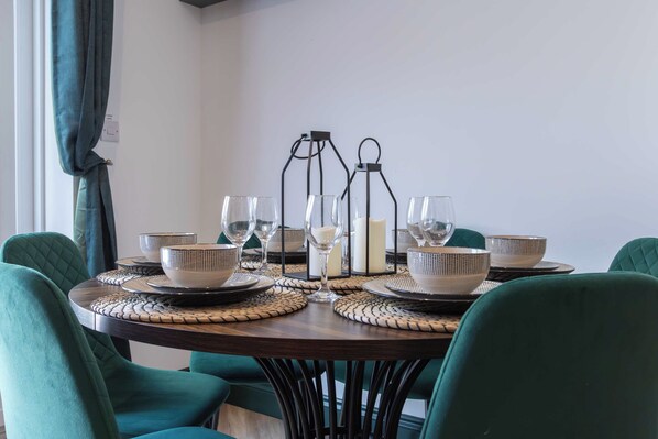 A dining table set with white and patterned bowls, glasses, and candles, surrounded by green upholstered chairs.