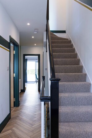 Un interior moderno con una escalera alfombrada, piso de madera y vista a una habitación luminosa.