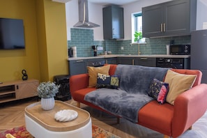 Un espacio habitable compacto con un sofá, una mesa de centro y una zona de cocina con microondas y armarios.
