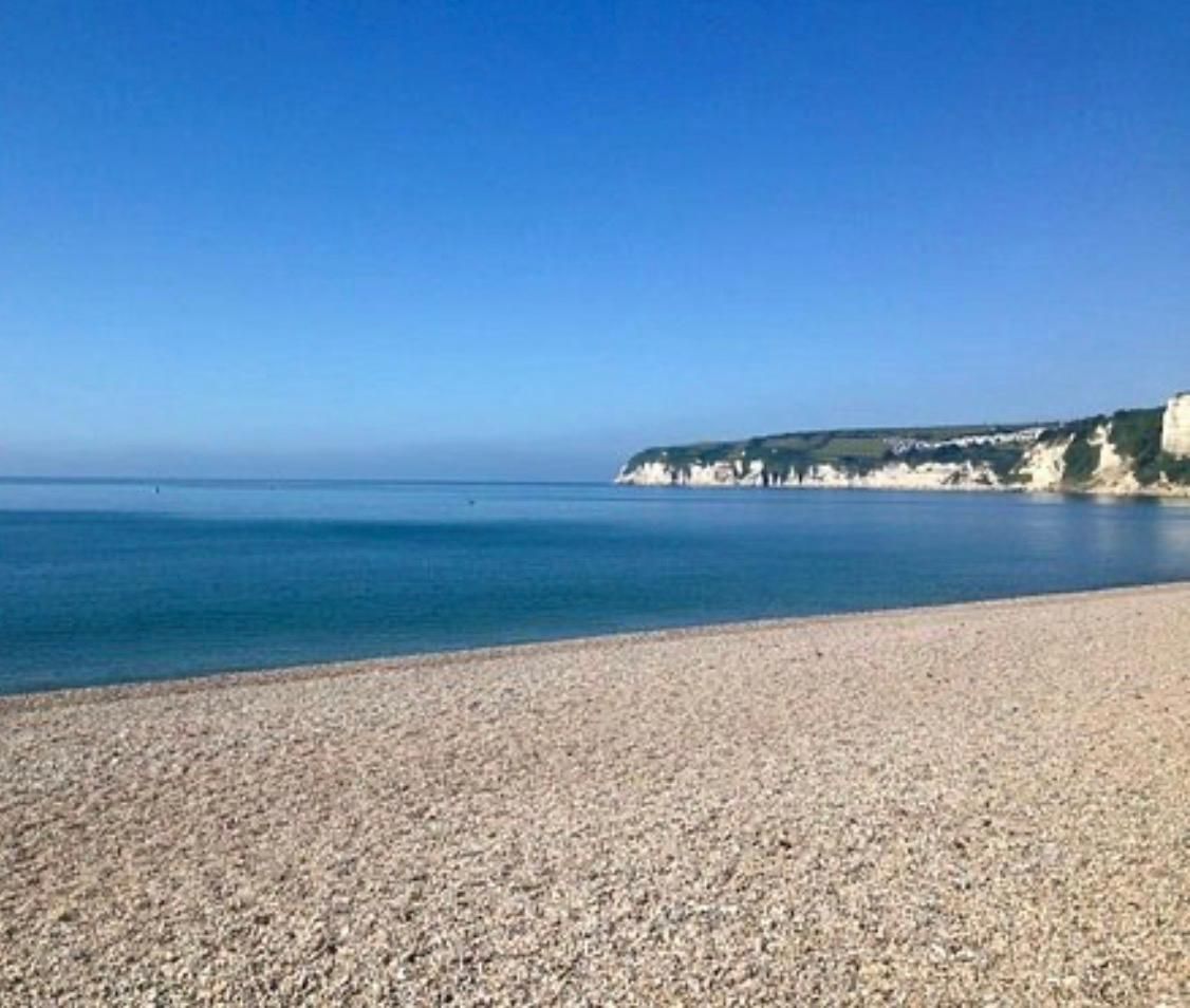 A pebble beach with a calm sea and cliffs in the background.