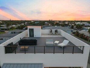 A rooftop terrace with a black sofa, a white lounge chair, and a small table. - Rooftop at 202 (New Smyrna Beach)