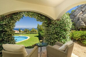 Un patio con mobiliario de mimbre, una mesa de vidrio y vistas a una piscina y paisaje.
