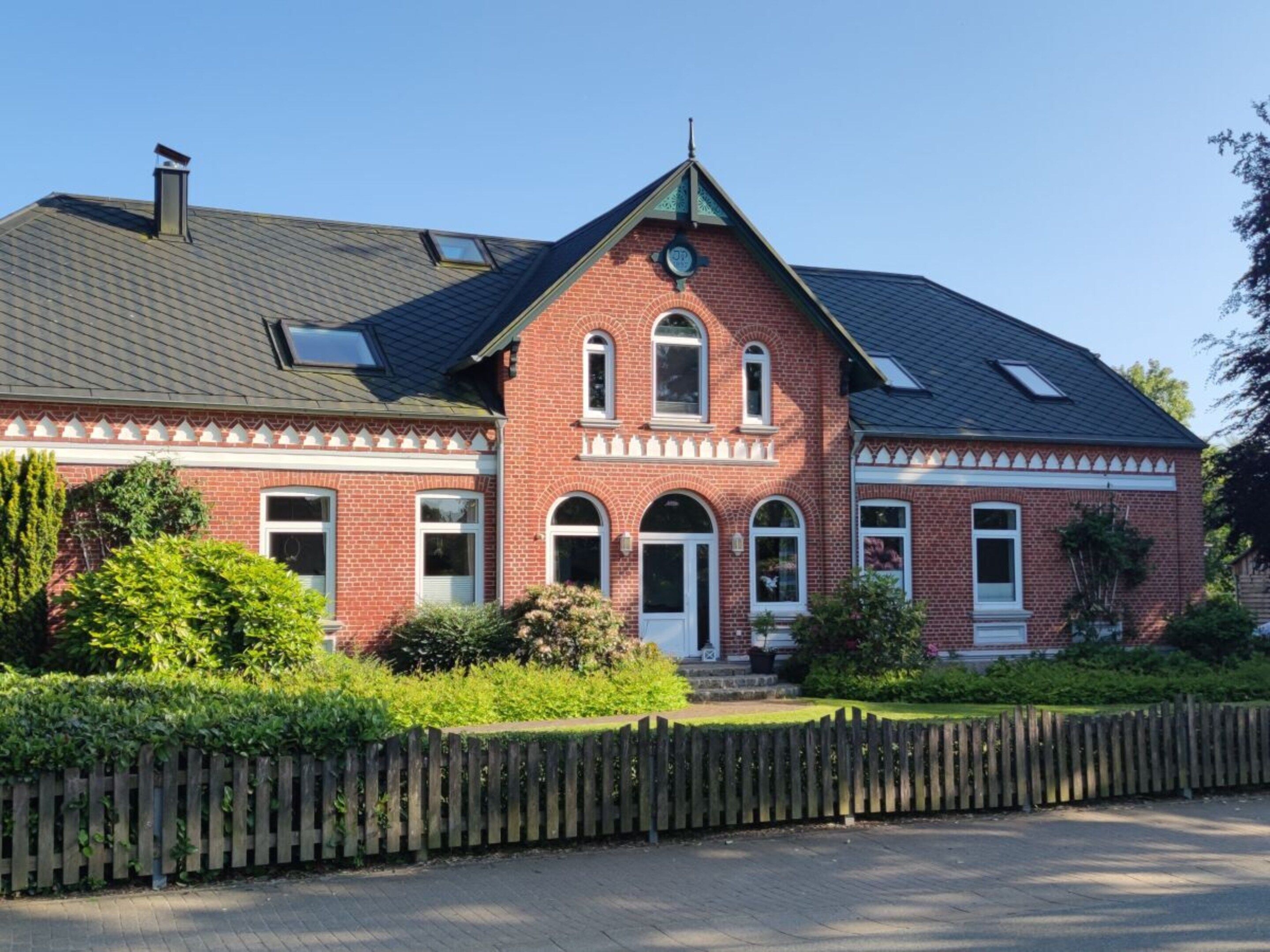 A red brick house with a gabled roof, a front porch, and a picket fence.