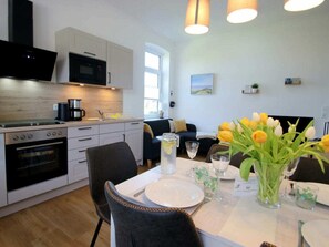 A modern kitchen with white cabinets, a black microwave, and a coffee maker. There is a dining table set with plates, glasses, and a vase of flowers. - Holiday Apartment With 1 Bedroom (Dollerup)