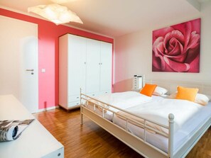A bedroom with a bed, a wardrobe, a nightstand, and a painting on the wall. - Holiday Apartment With 2 Bedrooms (Norderney)