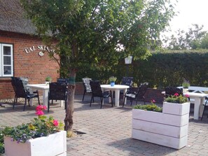 An outdoor seating area with tables and chairs, a brick building with a sign, and potted plants. - Holiday Apartment With 2 Bedrooms (Utersum)