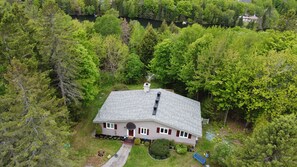 Une maison avec un toit en pente, entourée d’une forêt dense.