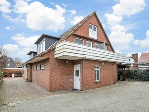 A two-story brick house with a balcony, a door, and a small garden area. - Holiday Apartment With 1 Bedroom (St. Peter-Ording)