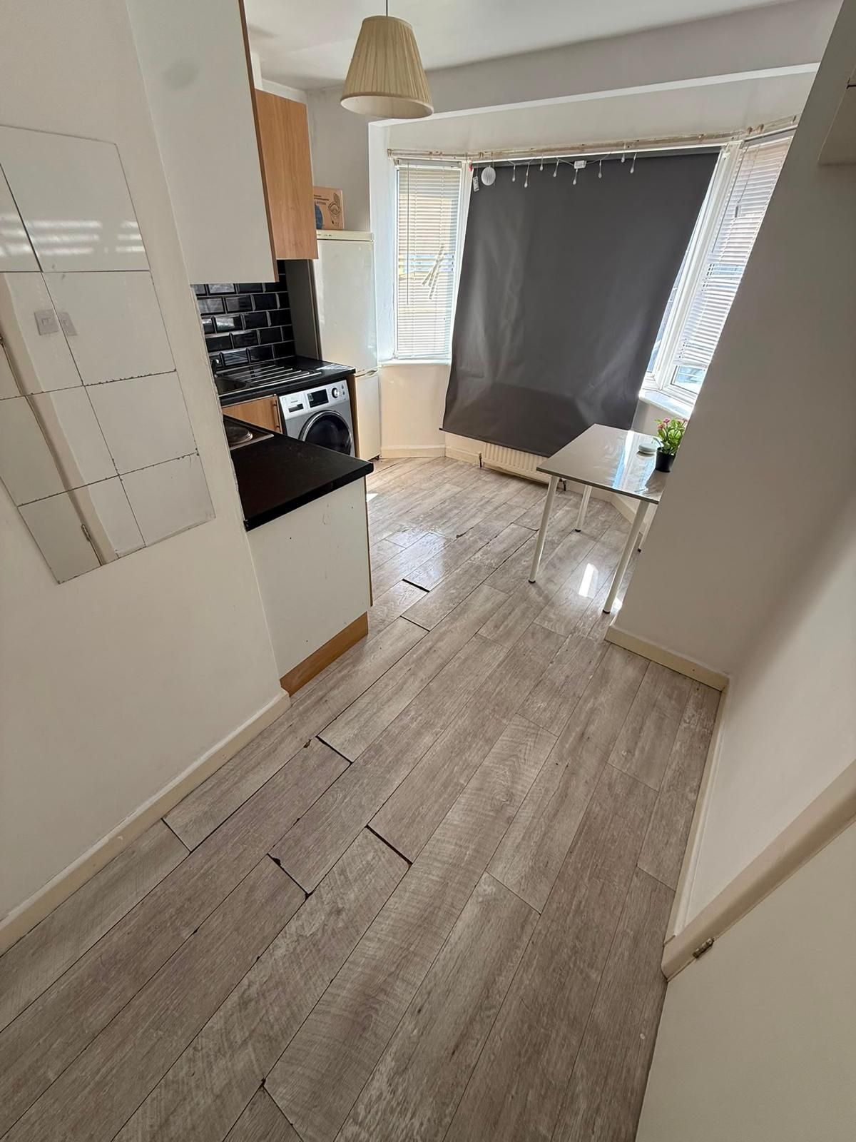 Une cuisine moderne équipée d’un lave-linge, d’un coin repas avec une table et d’une fenêtre avec des stores.