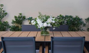 A dining table with chairs, a vase of white flowers, and a backdrop of green foliage. - STUNNING 5-BEDROOM HOME WITH PRIVATE TERRACE & PIAZZA VIEWS (Firenze)