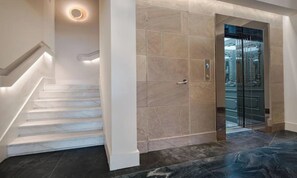 A modern interior with a marble staircase, a glass elevator, and a light fixture on the wall. - STUNNING 5-BEDROOM HOME WITH PRIVATE TERRACE & PIAZZA VIEWS (Firenze)