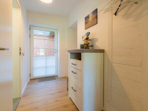 Ein Flur mit Holzboden, einer weißen Tür mit Fenster und einem an der Wand befestigten Regal mit Dekoration.