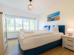 Une chambre à coucher avec un grand lit, une table de chevet, un tableau et une fenêtre avec des stores.