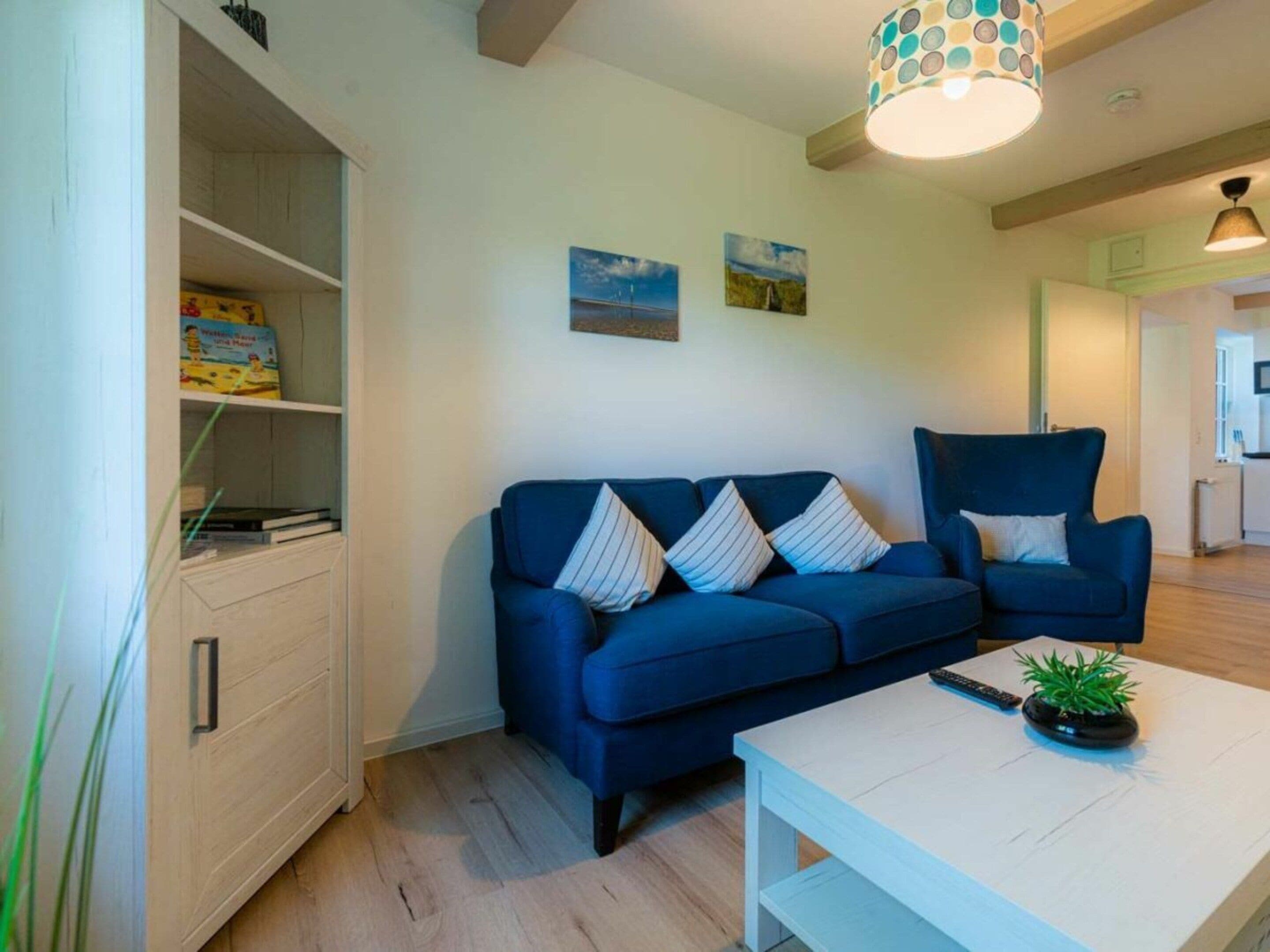 Una sala de estar con un sofá azul, una mesa de centro blanca y una estantería.