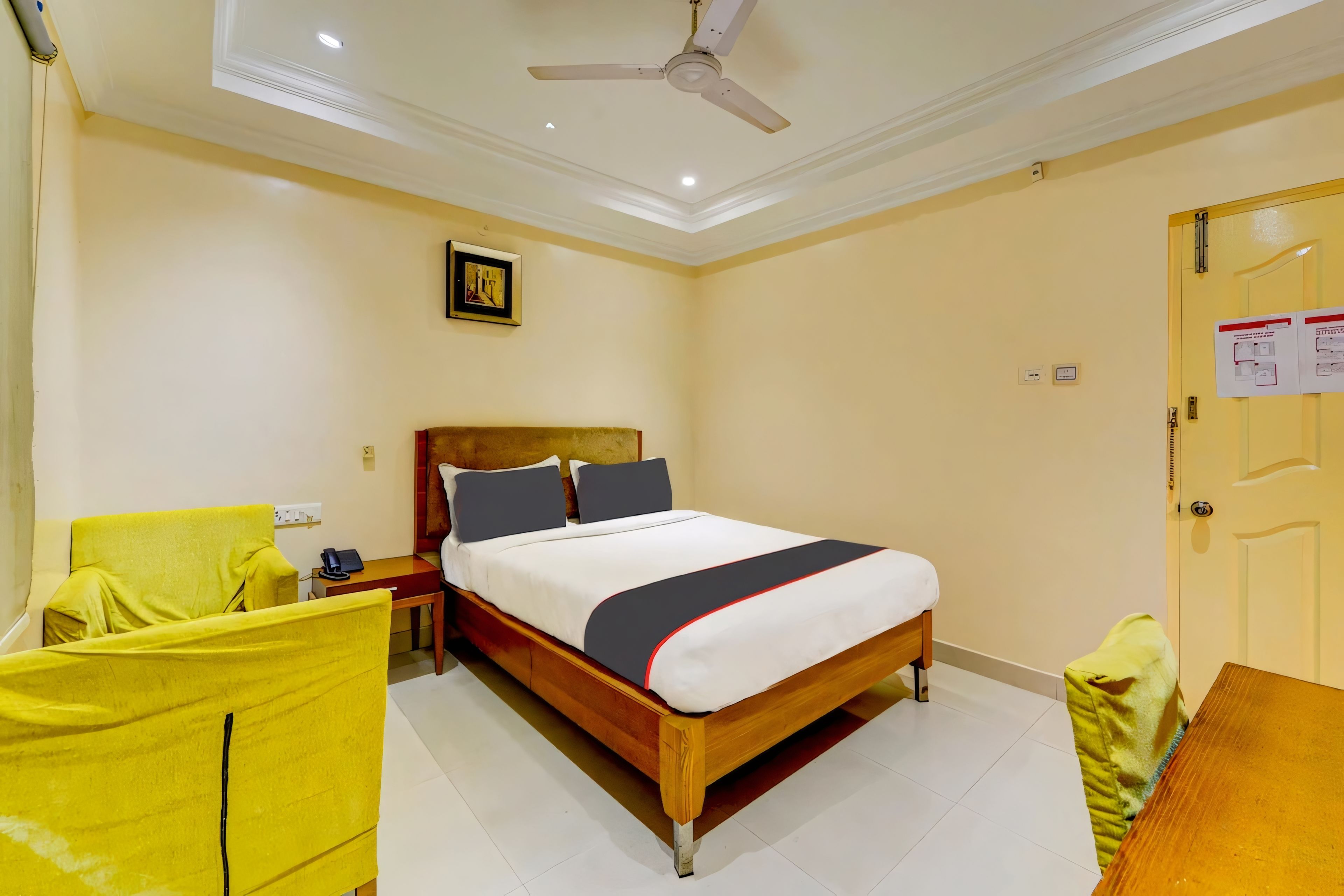 Una habitación de hotel con cama, escritorio, silla, ventilador de techo y puerta.