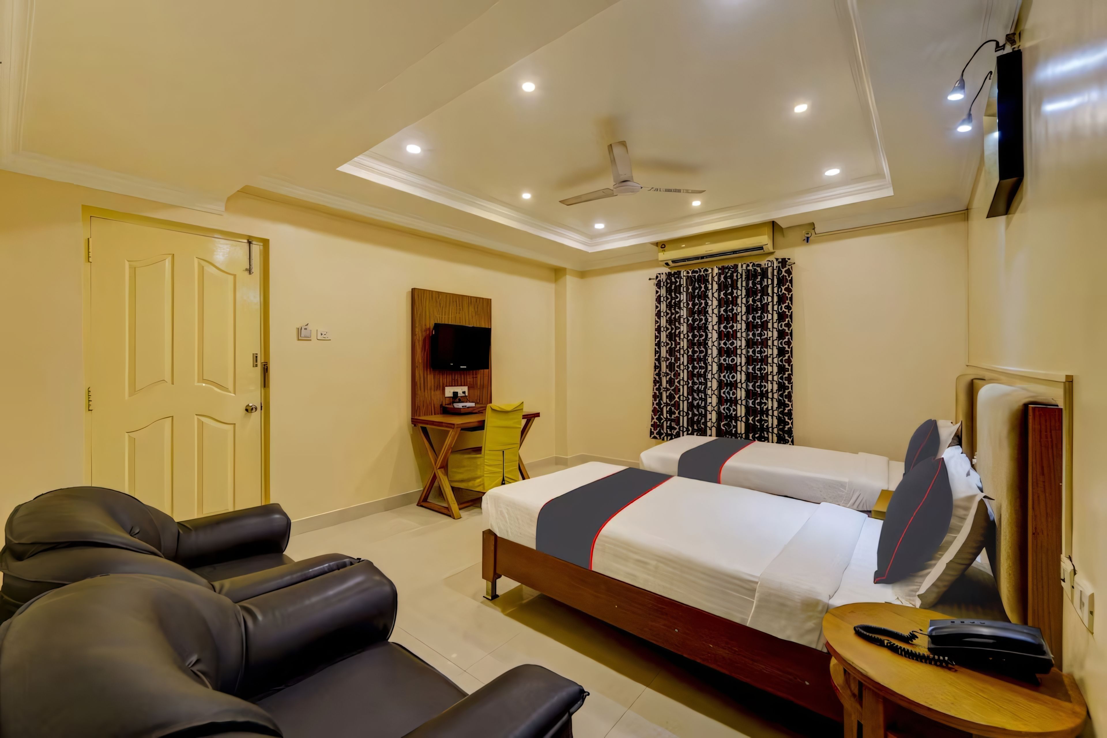 A hotel room with a bed, a desk, a chair, a sofa, and a ceiling fan.