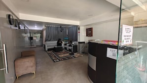 Habitación de hotel con sofá, una mesita, un ventilador y un panel de vidrio con un letrero.