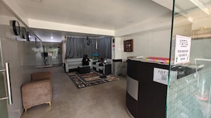 A hotel room with a sofa, a small table, a fan, and a glass partition with a sign. - XOTEL ASHOKNAGAR (Chennai)