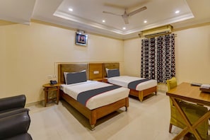 A hotel room with two beds, a desk, a chair, a ceiling fan, an air conditioning unit, and a curtain with a geometric pattern. - XOTEL ASHOKNAGAR (Chennai)
