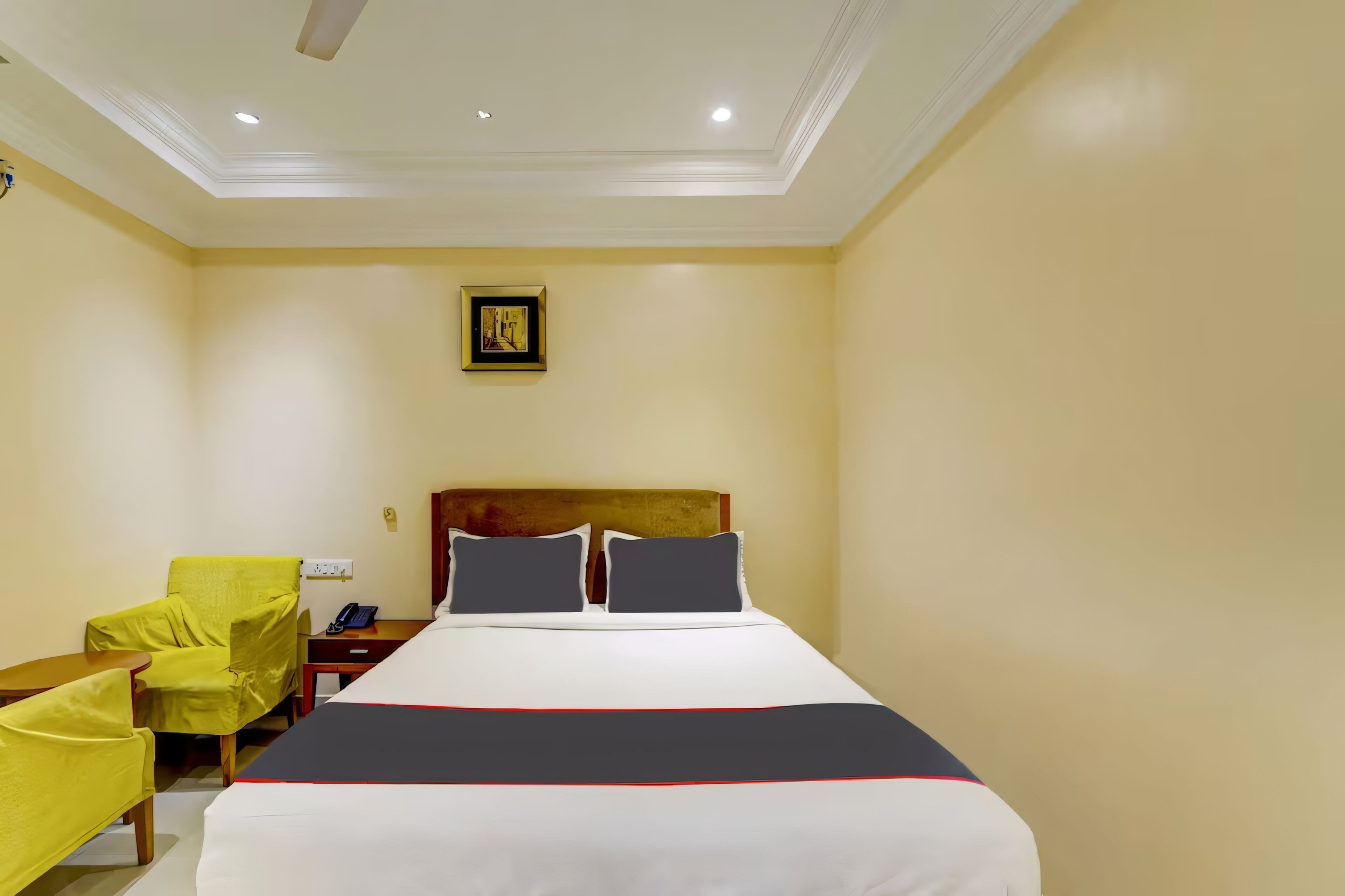 A hotel room with a bed, a chair, a nightstand, and a wall-mounted picture.