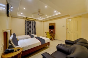 A hotel room with two beds, a desk, a chair, a sofa, and a TV.