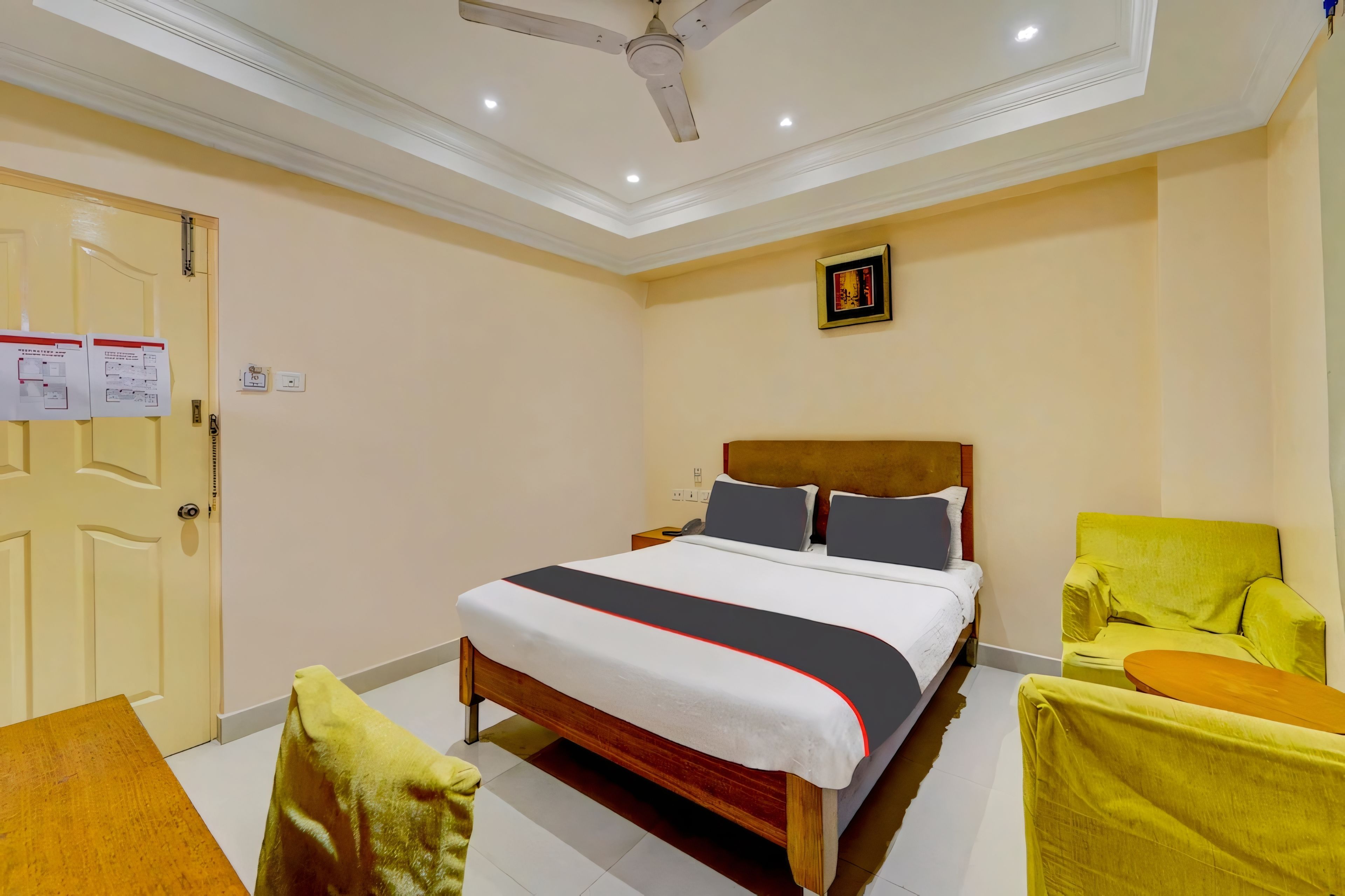 A hotel room with a bed, a chair, a desk, and a ceiling fan.