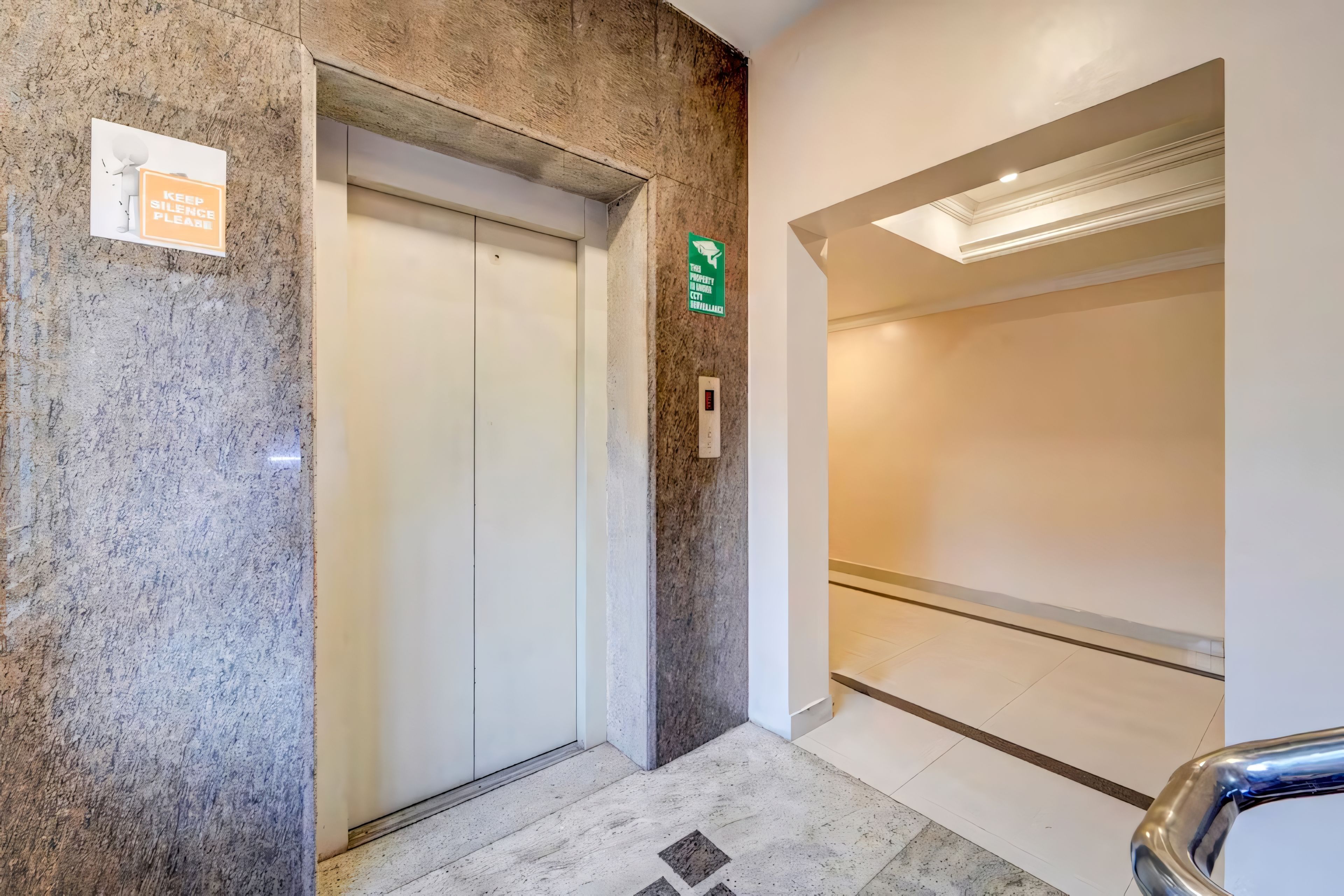 Un ascensor con un cartel que indica uso exclusivo para empleados, un letrero de salida de incendios, y un interior limpio y moderno con suelo de mármol.
