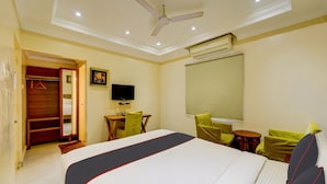 Habitación de hotel con cama, escritorio, silla, televisión y ventilador de techo.