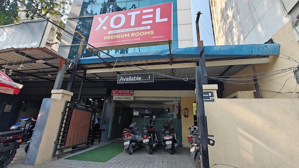 Entrada de un hotel con un cartel llamativo que dice 'XOTEL PREMIUM ROOMS' y una pantalla digital que muestra la disponibilidad.