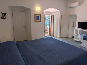 Une chambre à coucher comprenant un lit, une télévision, une armoire et une porte donnant sur un balcon extérieur.