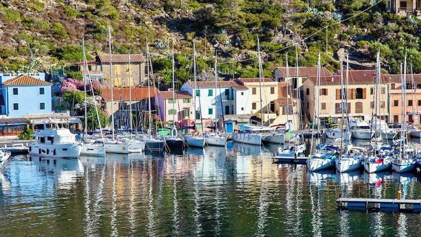 Un puerto deportivo con barcos amarrados, rodeado de edificios con tejados rojos.