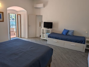 A bedroom with two beds, a TV on a stand, and a door leading to a balcony.