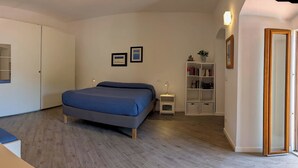 Un dormitorio con cama, armario, mesilla de noche, estantería y puerta.