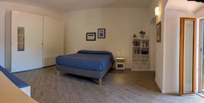 Een slaapkamer met een bed, een kledingkast, een nachtkastje, een boekenplank en een deur.