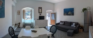 Een moderne woonkamer met een eethoek, een bank, een televisie en een keuken met een koelkast.