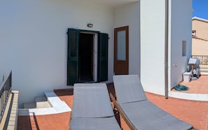 Een balkon met twee loungestoelen, een deur met groene luiken en een klein tafeltje.