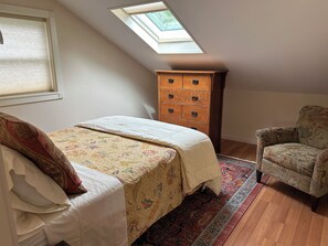 Ein Schlafzimmer mit einem Bett, einer Holzkommode, einem Stuhl und einem Oberlicht.
