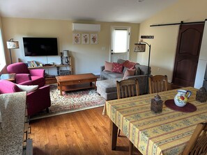 Una sala de estar con un sofá, sillones, una mesa de centro, un televisor y un comedor con una mesa y sillas.