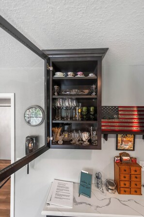 Une pièce avec un buffet en bois sombre contenant de la verrerie et de la vaisselle, une horloge au mur et un drapeau américain encadré.