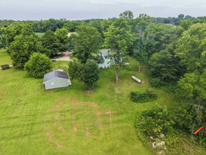 Une propriété rurale comprenant un grand champ ouvert, une petite maison et de nombreux arbres qui l’entourent.