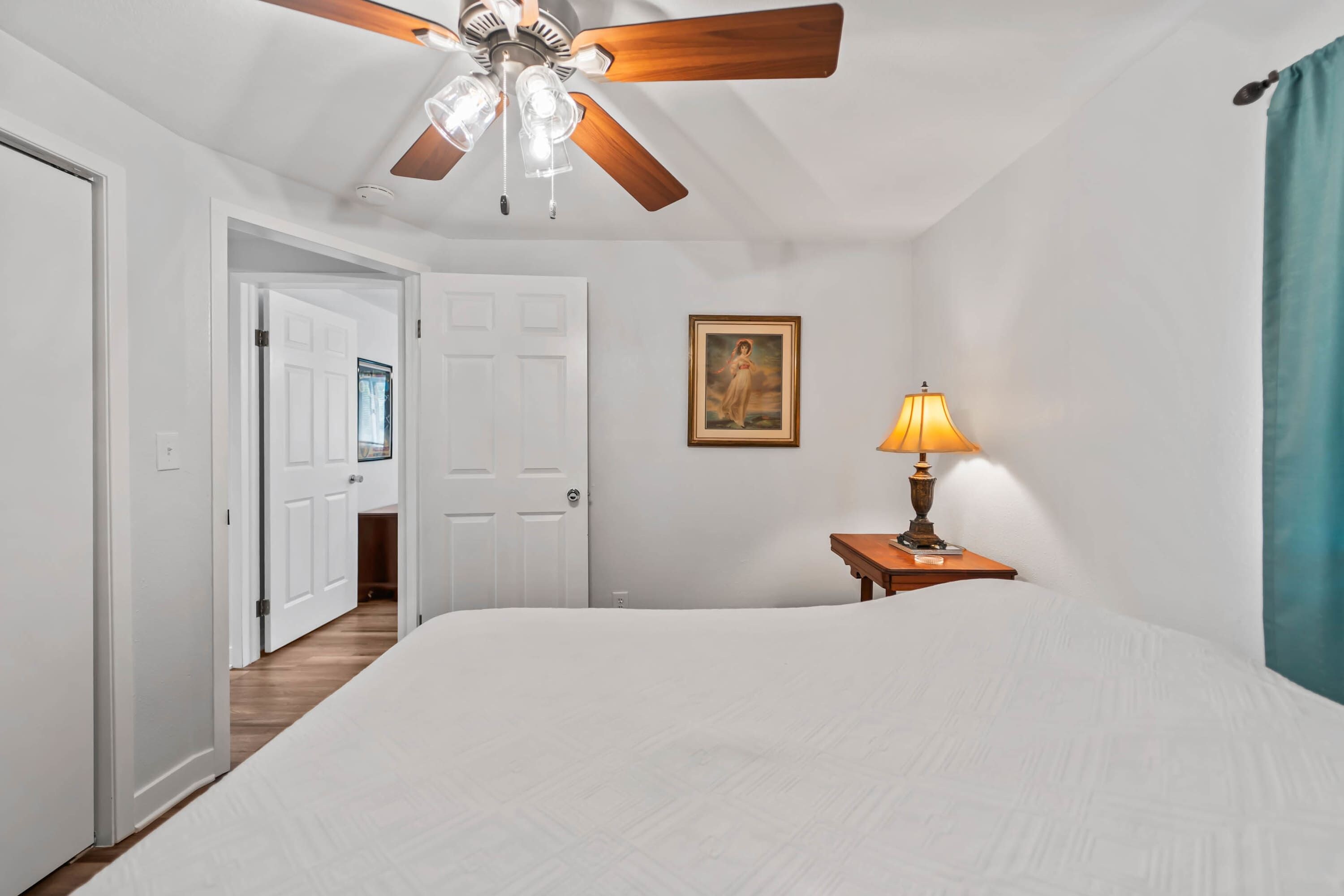 Une chambre à coucher avec un grand lit, un ventilateur de plafond, un tableau au mur et une table de chevet avec une lampe.