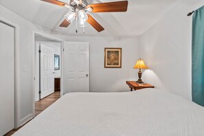 Une chambre à coucher avec un grand lit, un ventilateur de plafond, un tableau au mur et une table de chevet avec une lampe.