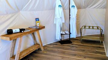 Interior de uma tenda com uma mesa de madeira, um porta-toalhas e uma cama portátil.