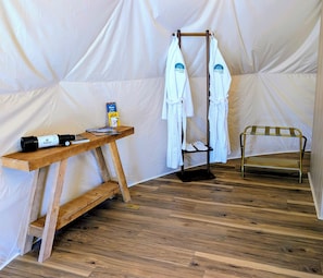 Interior de uma tenda com uma mesa de madeira, um porta-toalhas e uma cama portátil.