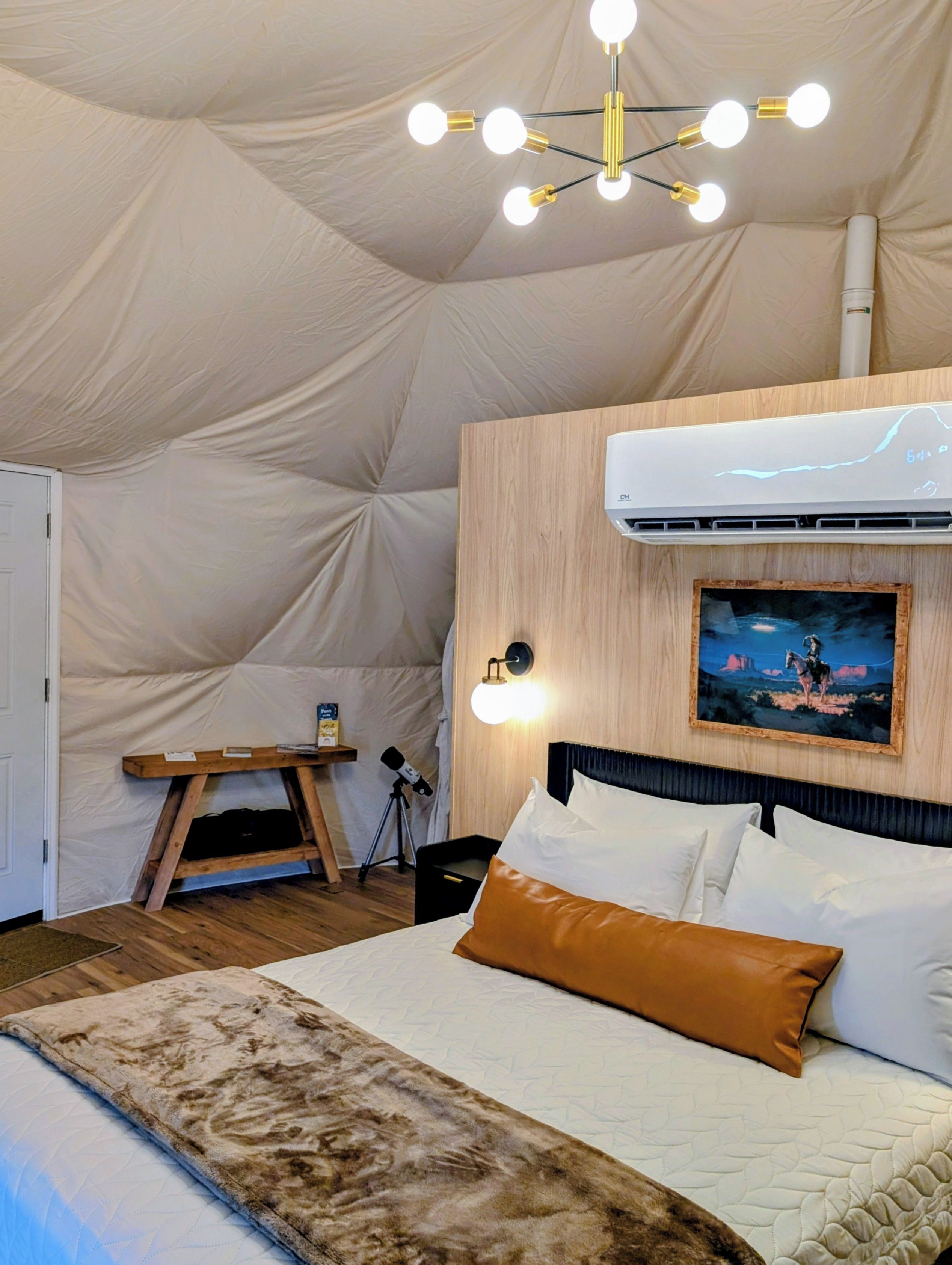 Quarto com tenda, uma cama, ar condicionado fixado na parede, um quadro pendurado e um tripé com câmera.