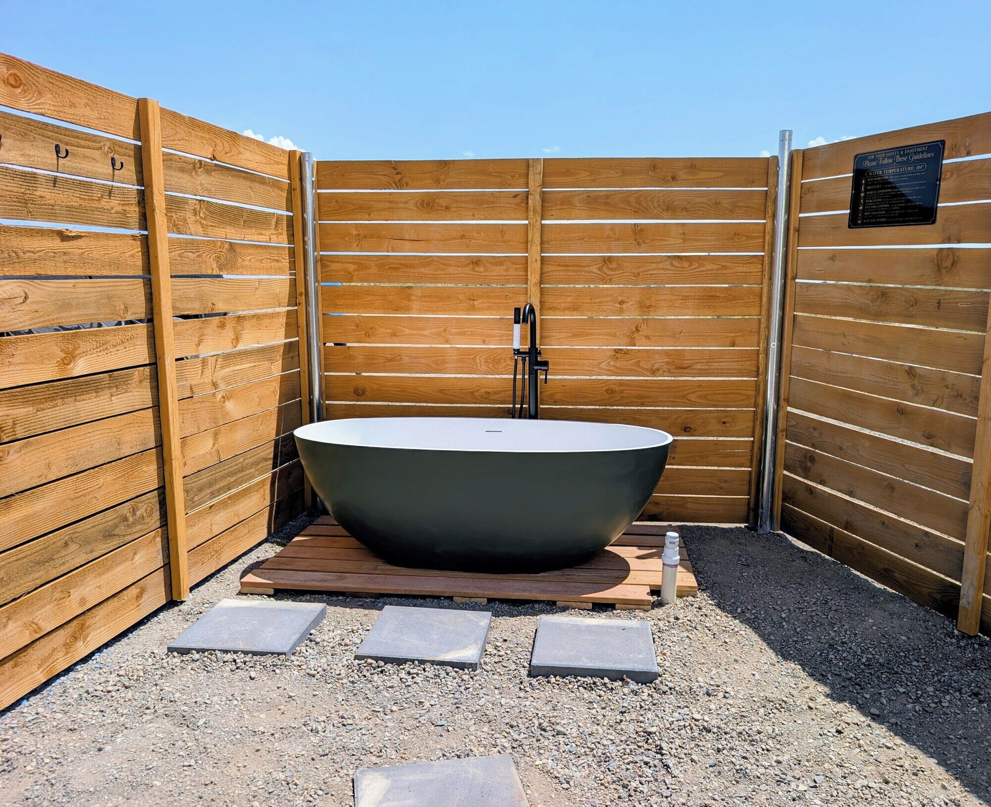 Un jacuzzi exterior independiente con diseño moderno, rodeado de vallas de madera y grava.