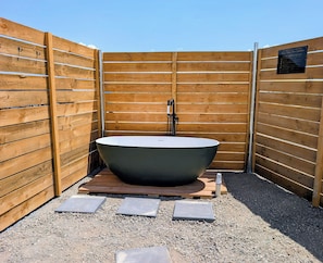 Uma banheira de hidromassagem ao ar livre, isolada, com design moderno, cercada por vedação de madeira e cascalho.