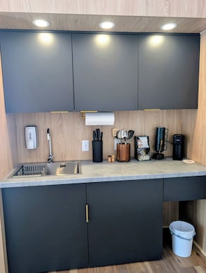 Uma cozinha moderna com armários escuros, uma pia de aço inoxidável e bancada com diversos utensílios e eletrodomésticos.