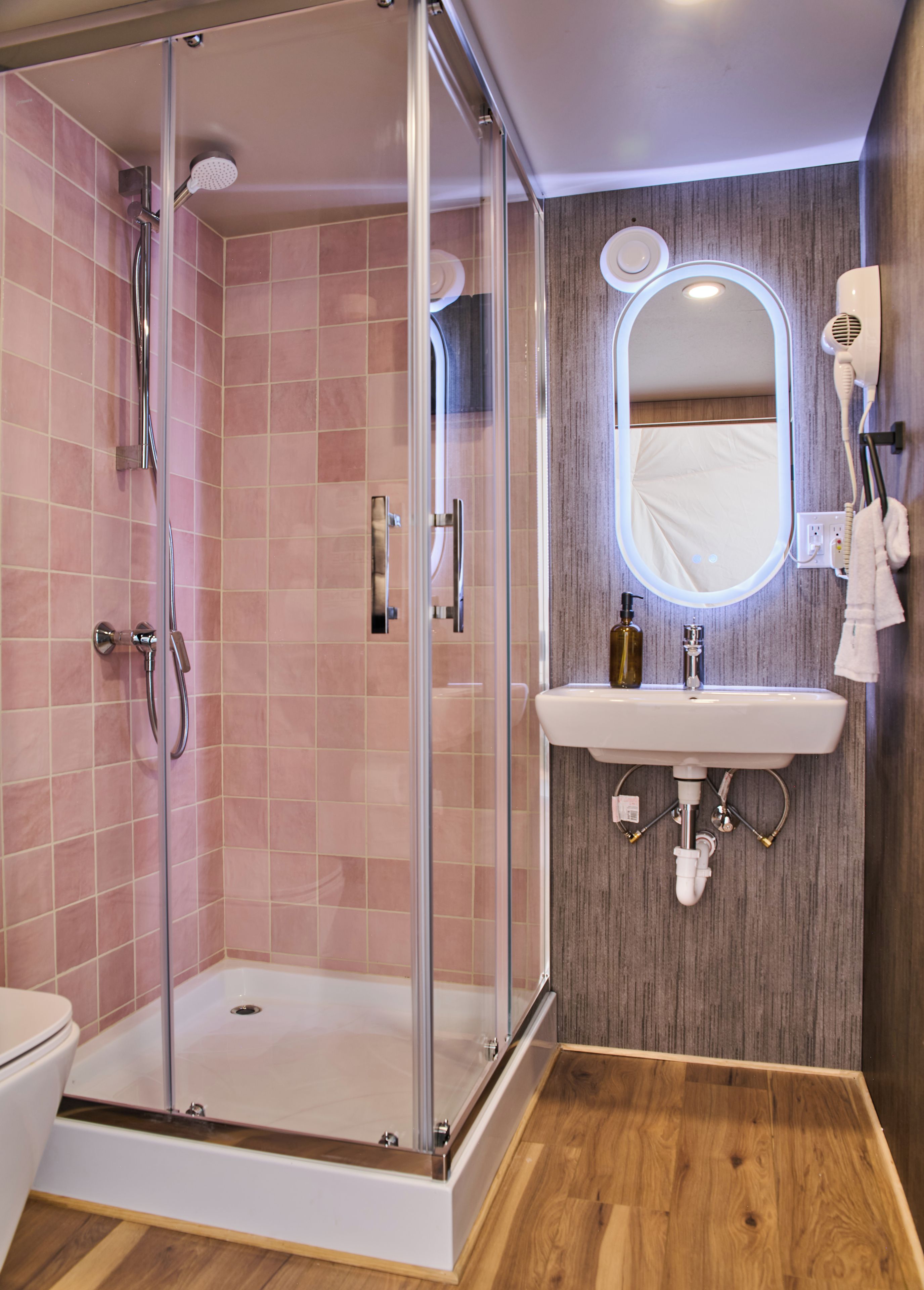 Une salle de bain moderne avec une douche à parois de verre, un plancher en bois et un lavabo surmonté d’un miroir.